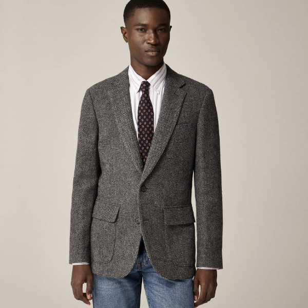 a man wearing a blazer over a dress shirt and tie and denim jeans