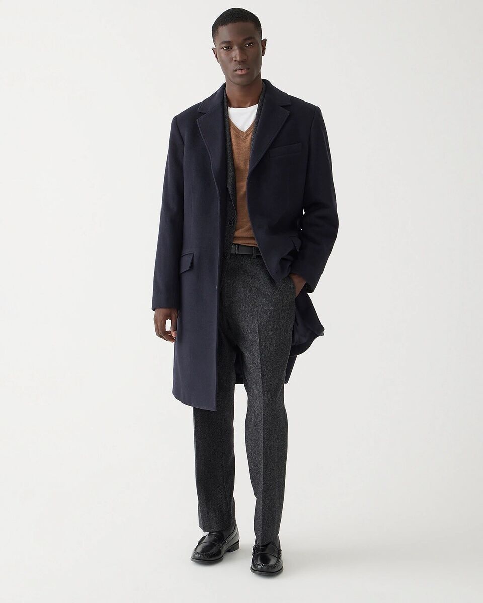 model for jcrew wearing a top coat over a v neck sweater and full cut dress trousers