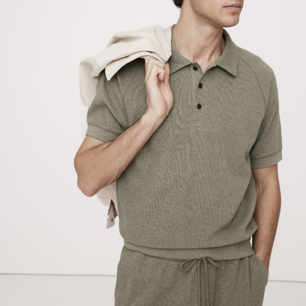 man wearing a waffle knit polo shirt over dress pants with a jacket slung over his shoulder