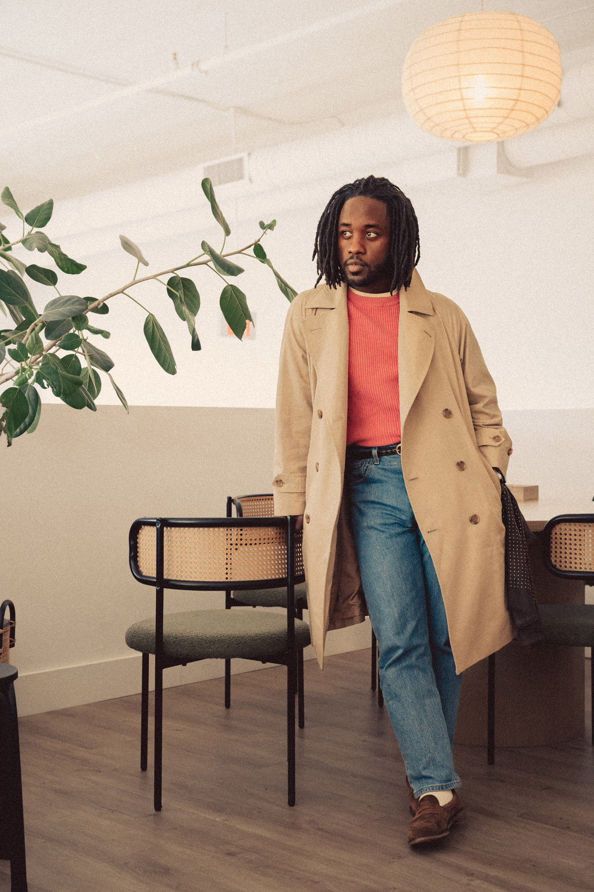 daniel wearing a trench coat, salmon sweater, light wash denim, and suede loafers