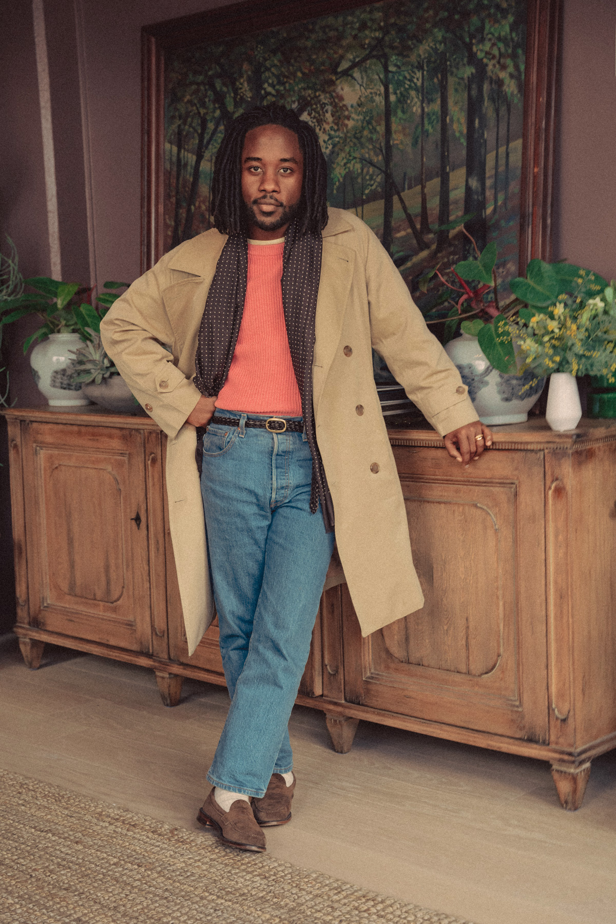 a man wearing a trench coat over a sweater with jeans