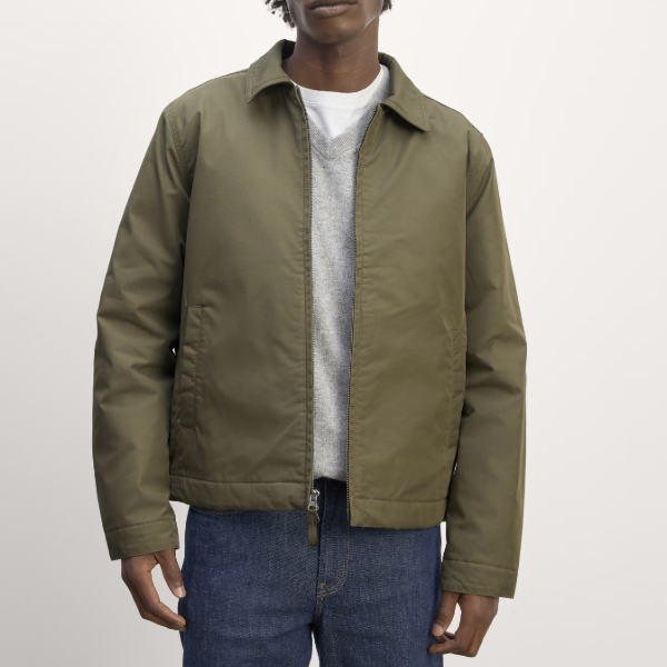 man wearing a harrington style jacket over a sweater and denim pants