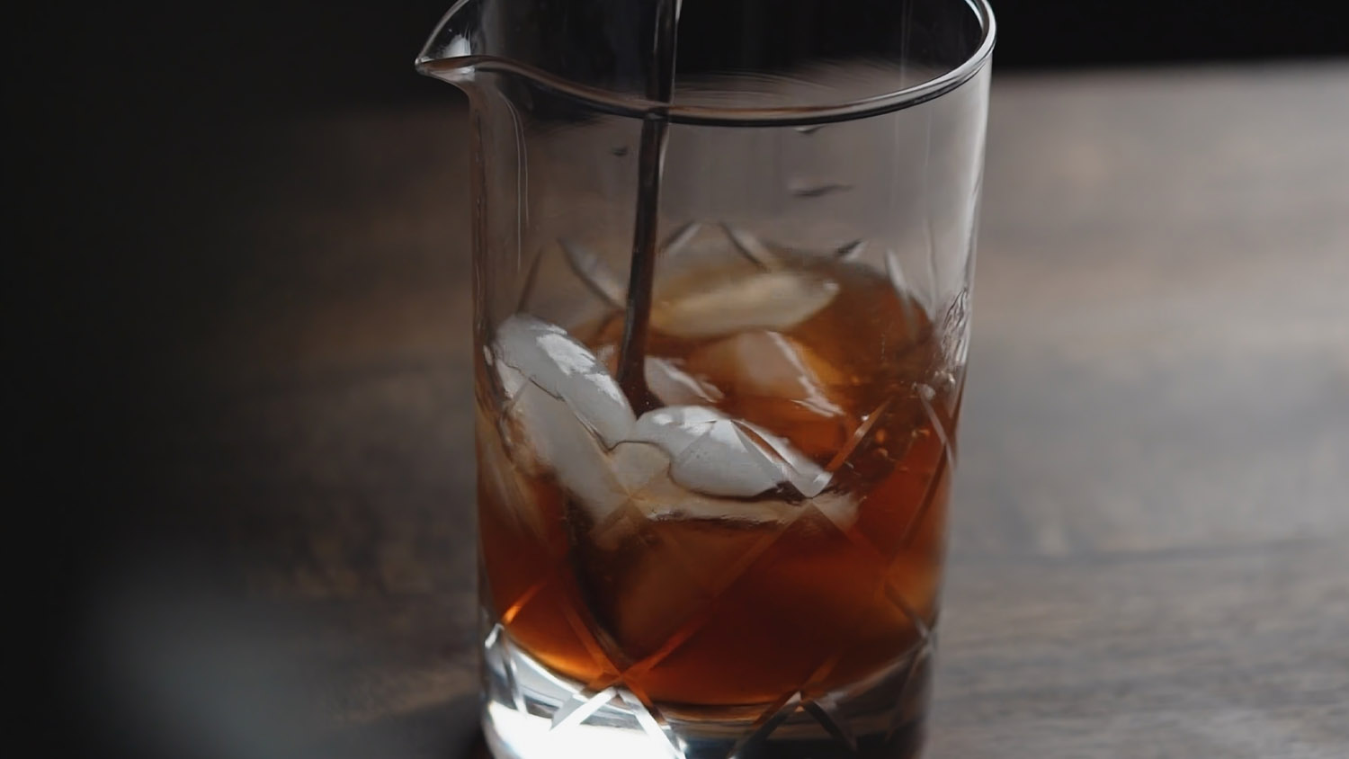 a crystal cocktail mixing glass filled with a beverage and ice