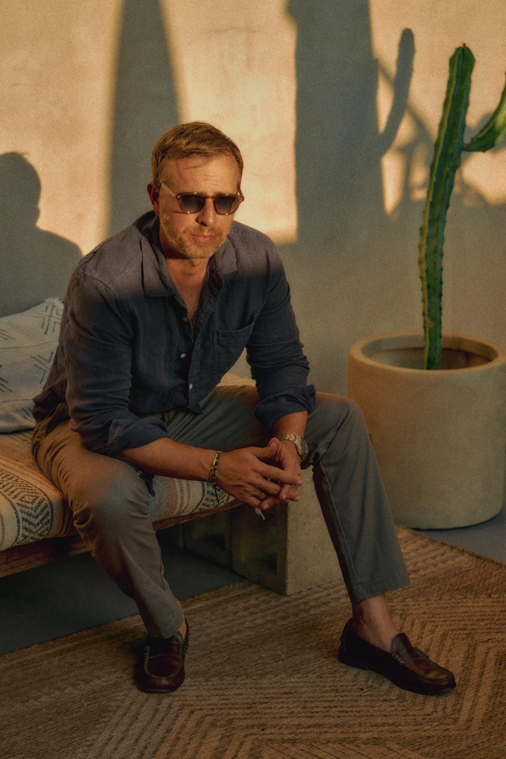 men's summer outfit of a blue linen shirt, stone chinos, brown loafers, a watch and sunglasses