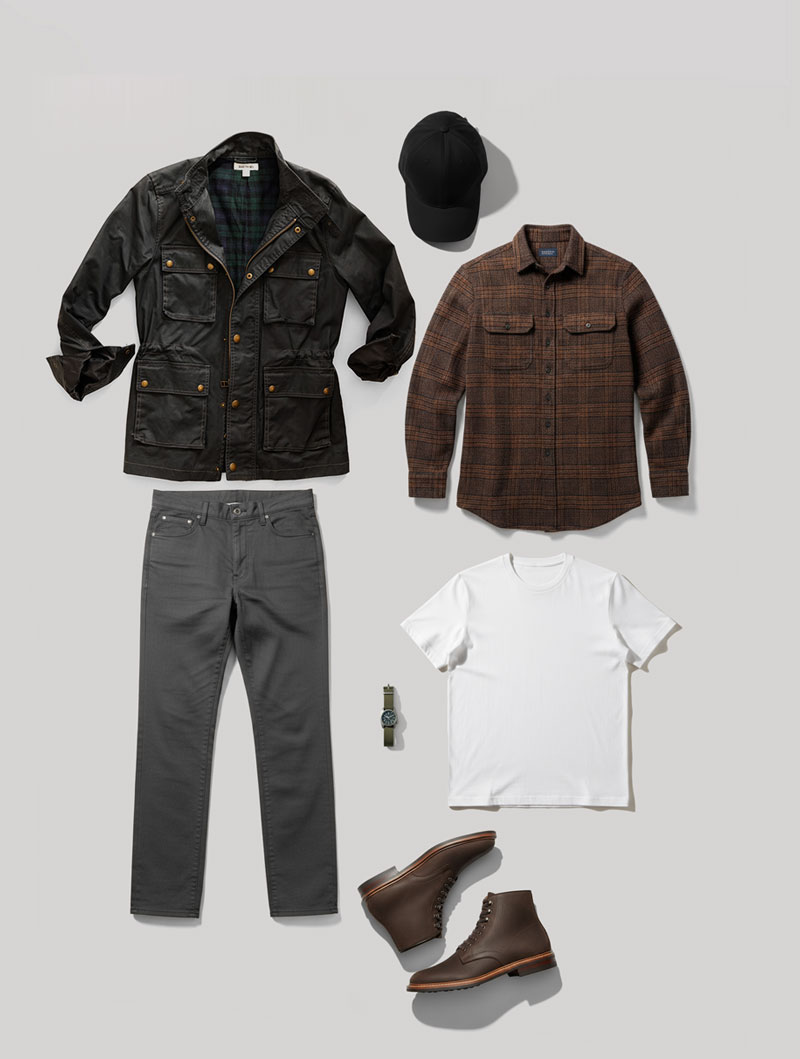 Fall-Men's-Outfit-Flannel-Waxed-Jacket_2-flat A flat lay display of a men’s smart casual outfit arranged on a light gray background. The items include a black utility jacket with gold snap buttons and a green plaid lining, a black baseball cap, a brown plaid flannel shirt, a plain white t-shirt, a pair of dark gray jeans, a silver wristwatch with a black face, and dark brown leather lace-up boots.