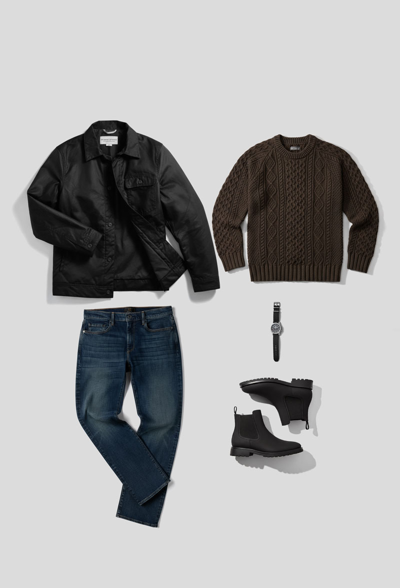fgw_2 Flat lay of a smart casual men's outfit arranged on a light gray background. The ensemble includes a black waxed canvas button-up jacket from Thursday Boot Co with a collar in the top left, a brown cable-knit crew neck sweater in the top right, a pair of medium-wash blue jeans folded at the knees in the bottom left, a black leather-strapped wristwatch in the center, and a pair of black Chelsea boots with rugged soles positioned in the bottom right.