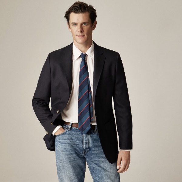 man wearing a navy blazer over a button up shirt and tie and denim jeans