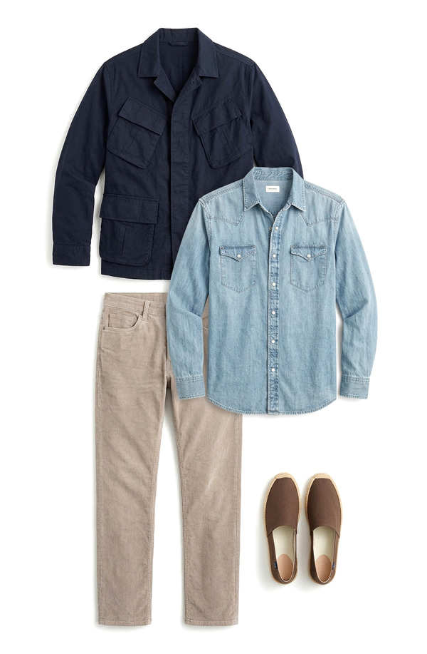 Men's smart casual outfit with a navy field jacket, light wash denim shirt, beige pants, and brown slip-on shoe